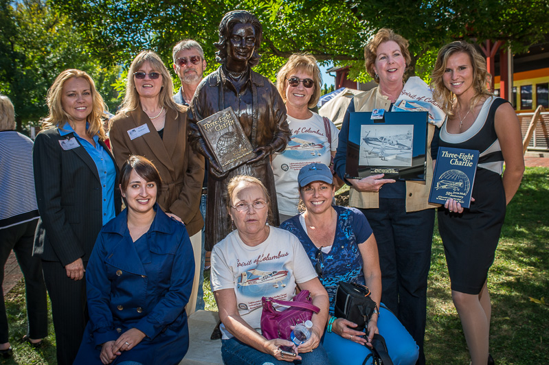women around a statue of woman pilot jerrie mock with a framed pencil drawing of her and her plane
